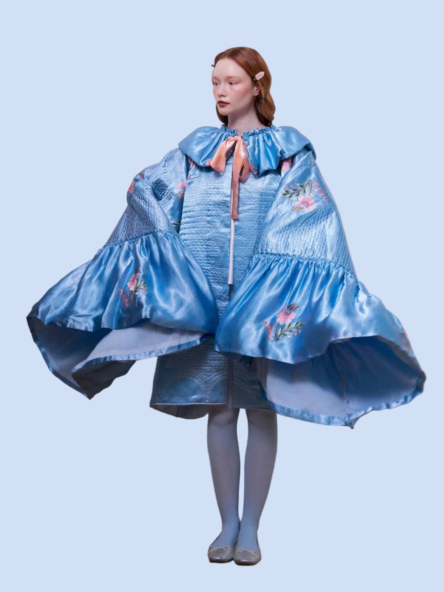 Woman wearing a blue embroidered dress with a cape against a plain background