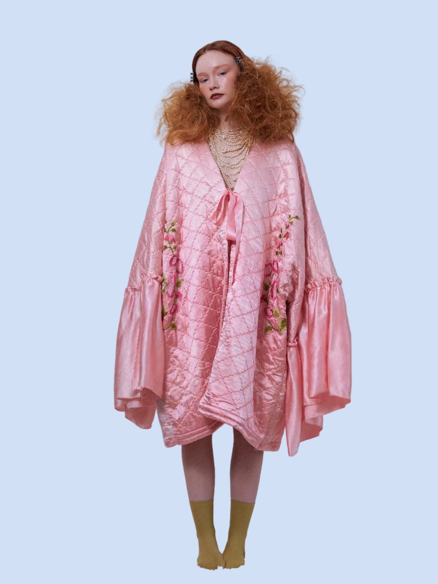 Woman wearing a pink quilted coat with floral patterns on a white background