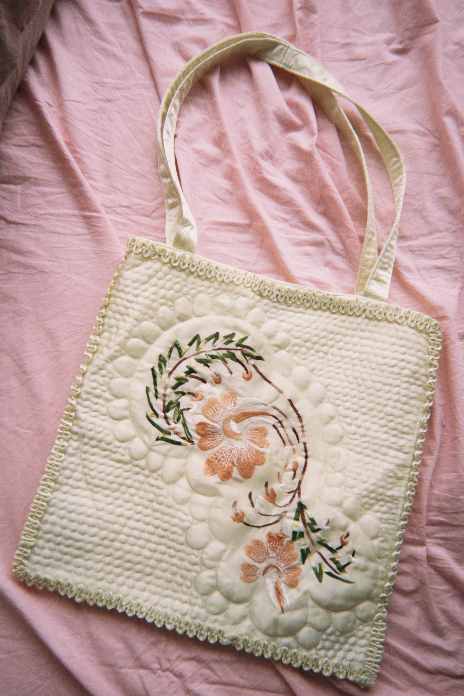 Embroidered tote bag with floral design on a pink fabric background