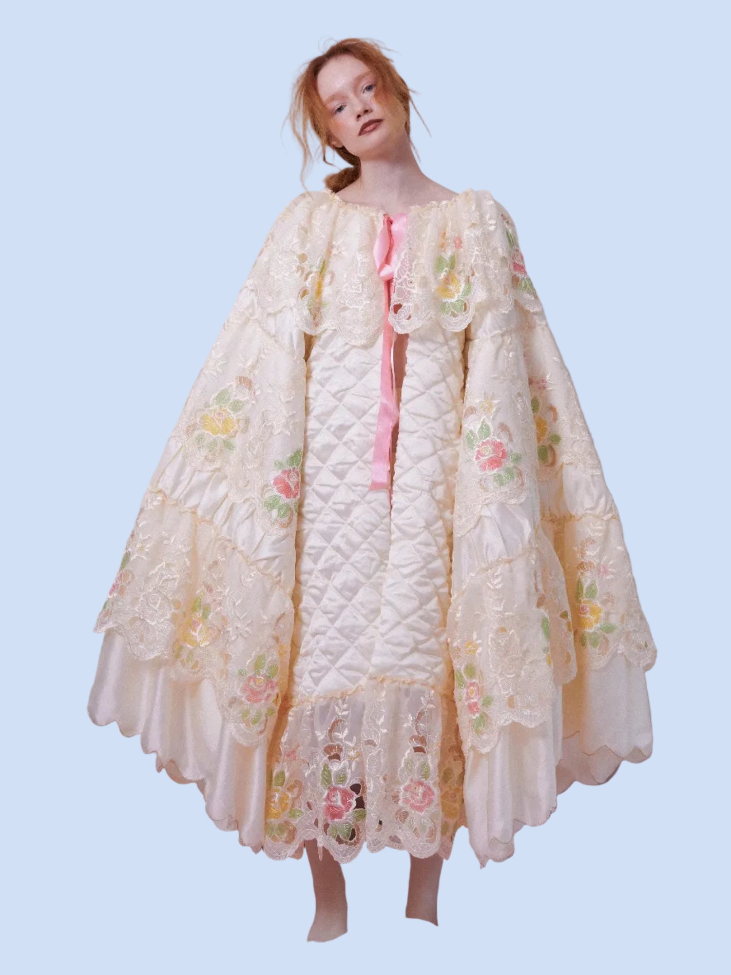 Woman wearing a floral lace nightgown on a bed with pink bedding.